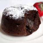 Close-up of a molten chocolate fondant with powdered sugar on top, served with a strawberry.